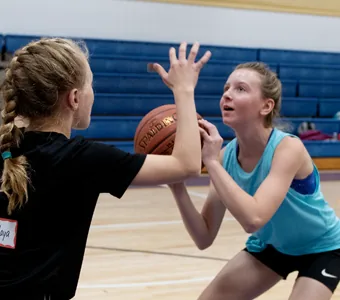 A girl holds a basketball up ready to shoot while a teammate raises a hand to defend.